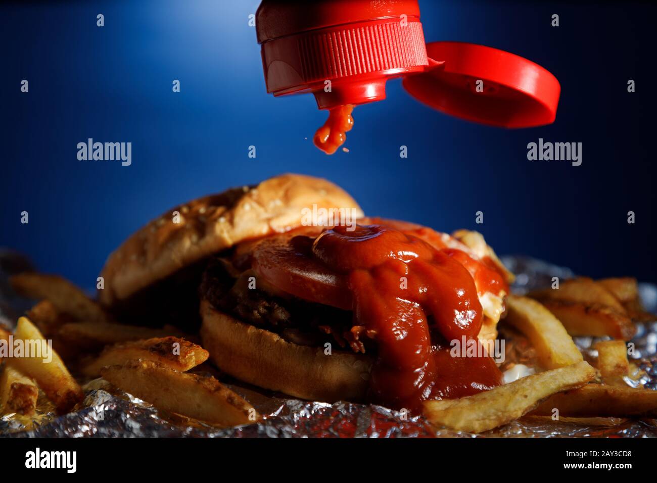 Putting ketchup on a hamburger and fries with a blue background Stock