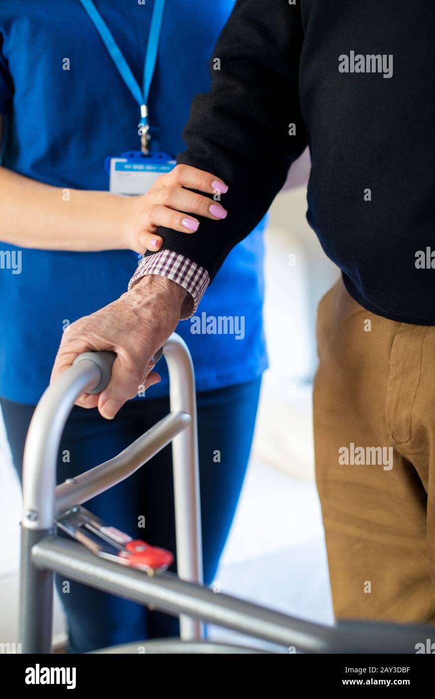 Close Up Of Senior Man With Hands On Walking Frame Being Helped By Care Worker Stock Photo