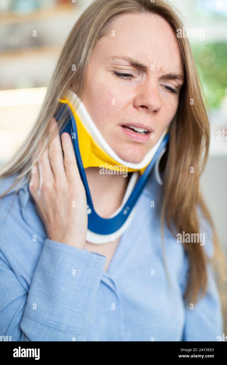 Woman Wearing Neck Brace At Home Winces With Pain Stock Photo