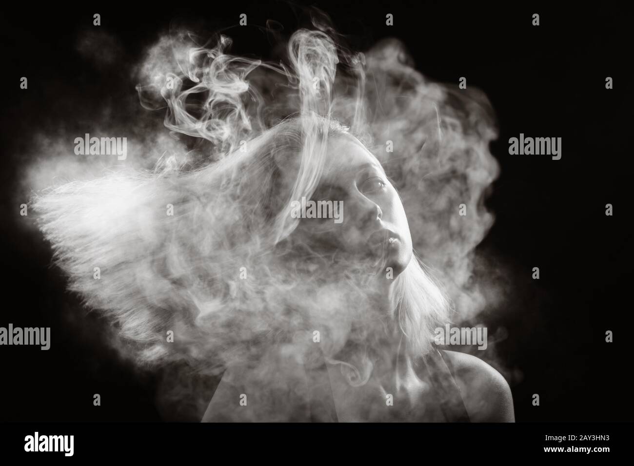 young blond woman dancing at white smoke cloud on black background, monochrome Stock Photo