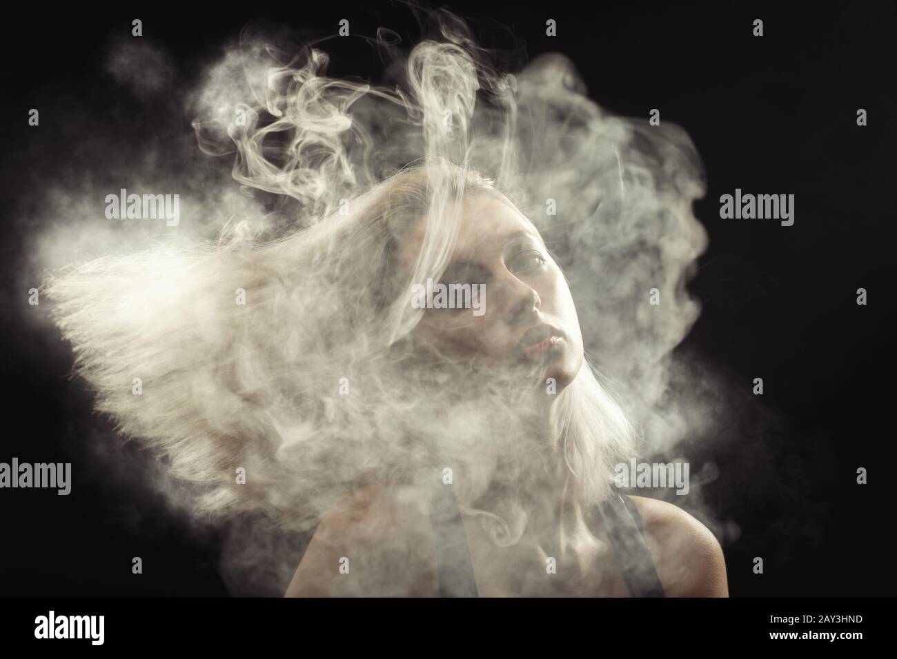 young blond woman dancing at white smoke cloud on black background Stock Photo