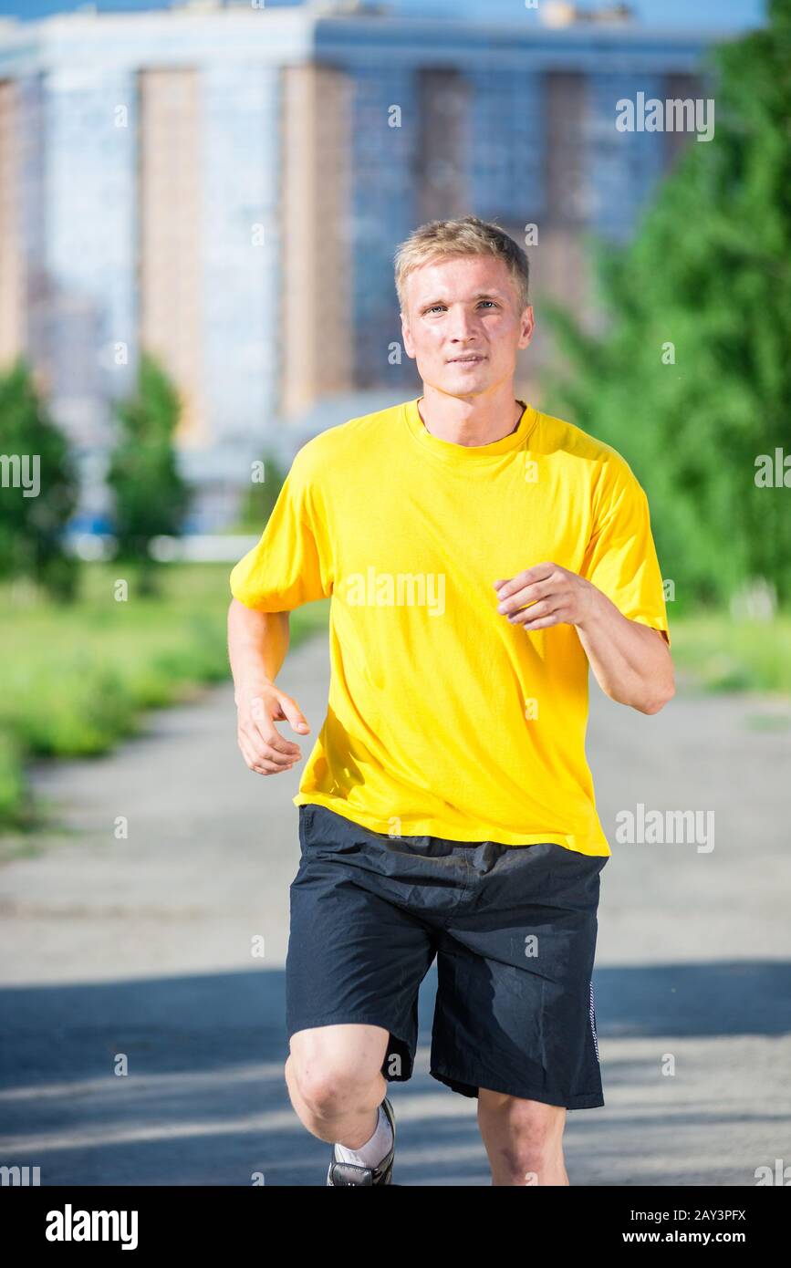 Sporty man jogging in city street park. Outdoor fitness. Stock Photo