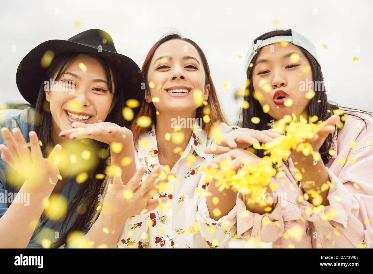 Happy Asian friends having fun throwing confetti outdoor - Young trendy people celebrating carnival festival event Stock Photo