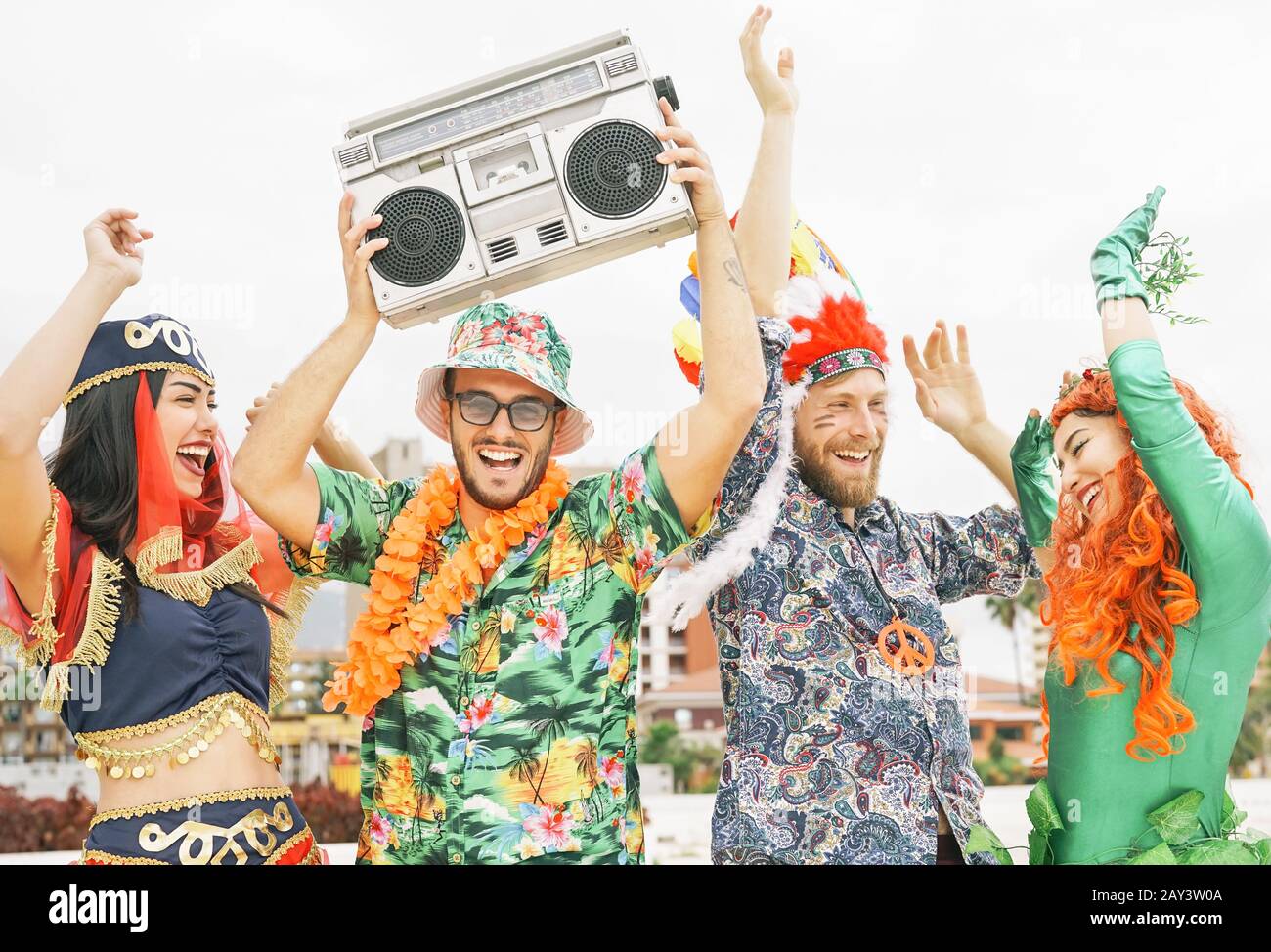 Happy friends celebrating carnival party outdoor - Young crazy people having fun wearing costumes listening music with vintage boombox stereo Stock Photo