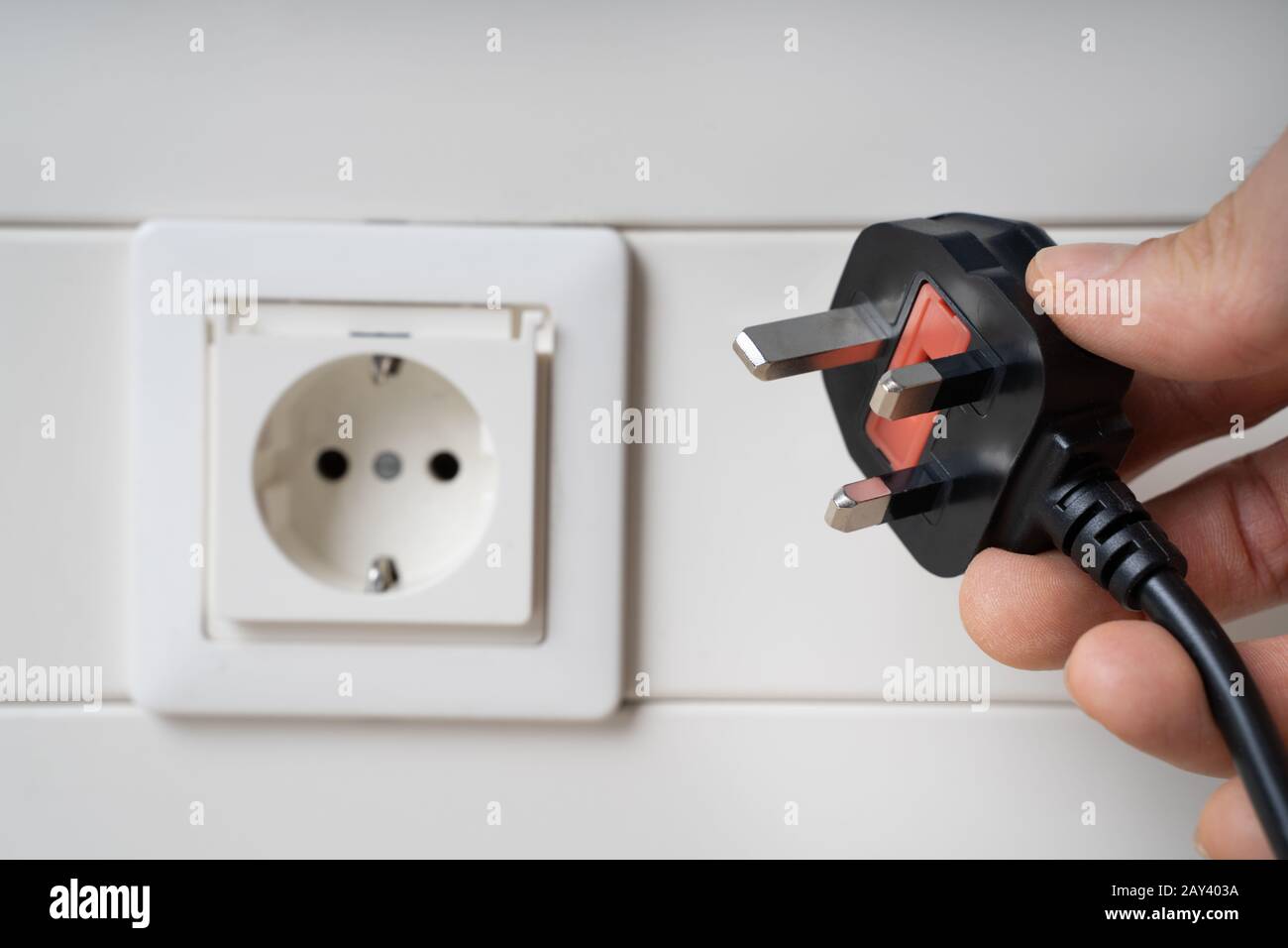 Hand Holding Incompatible AC Plug Near Wall Socket Stock Photo