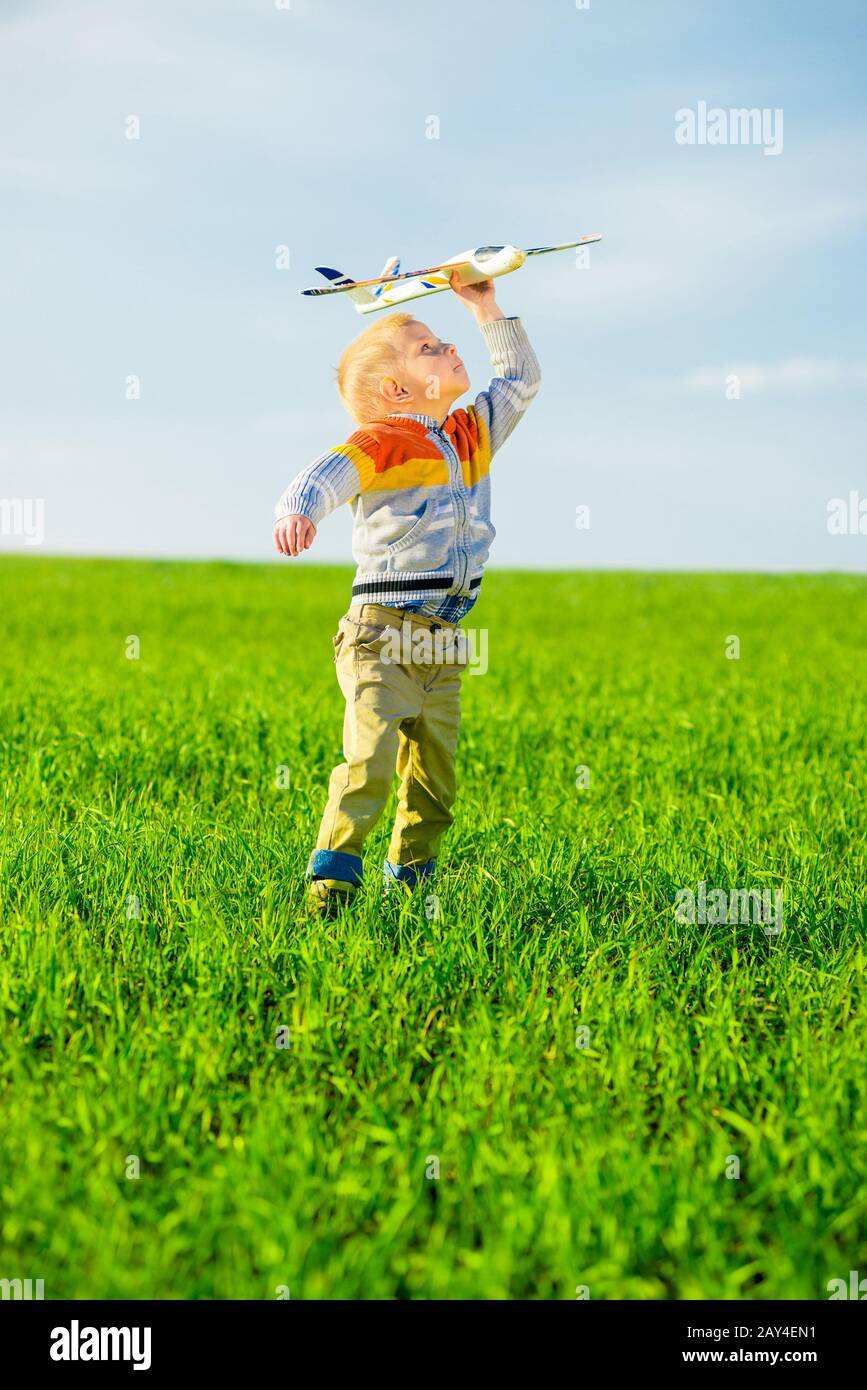 Happy boy playing with toy airplane against blue summer sky and green ...