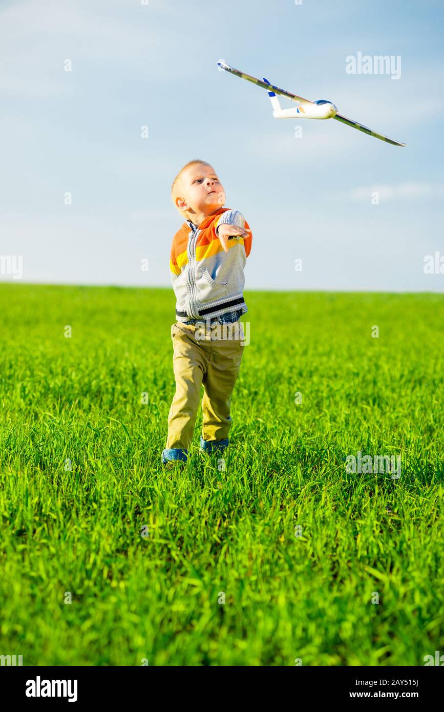 Happy boy playing with toy airplane against blue summer sky and green ...