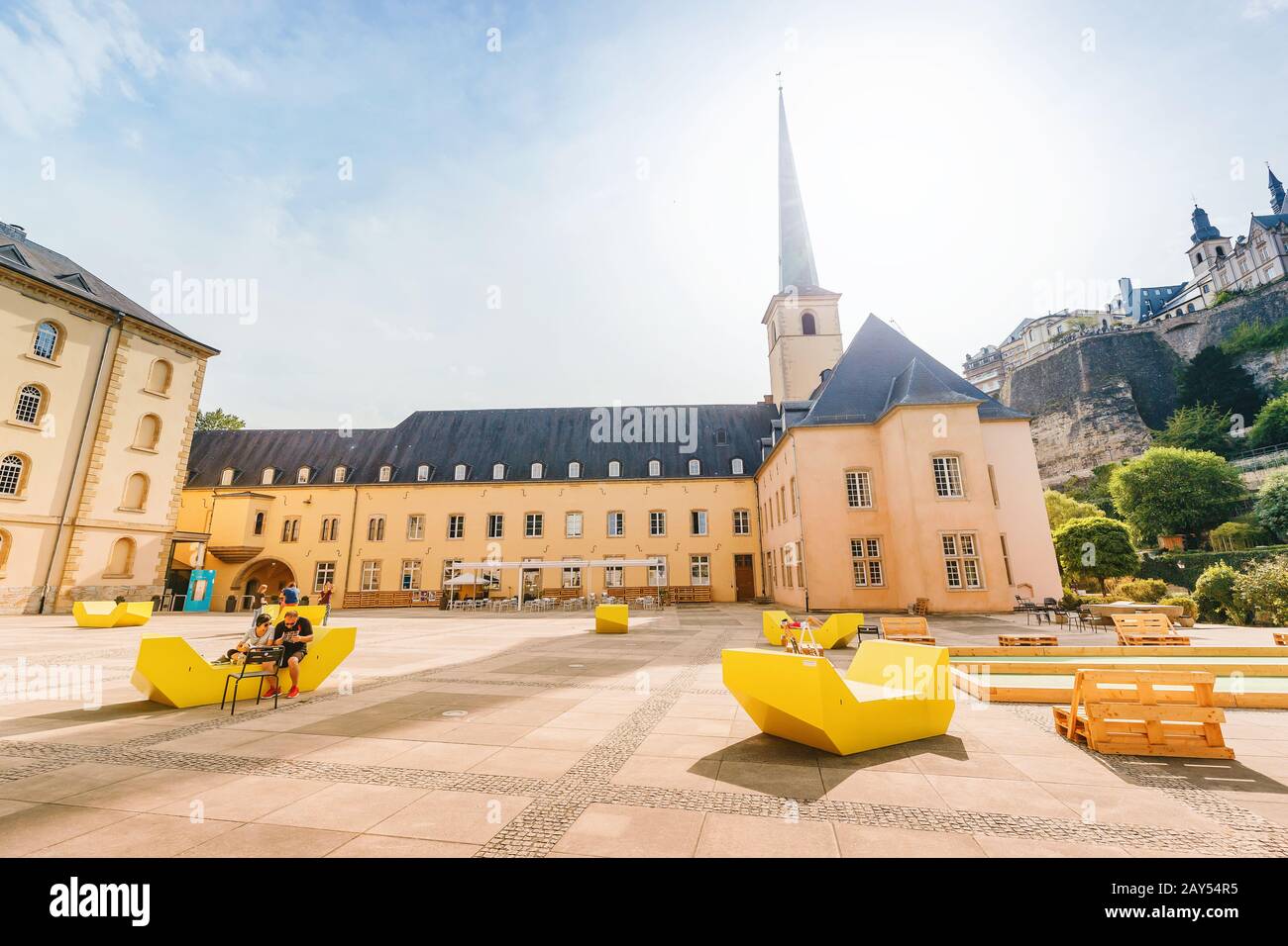 1 August 2019, Luxembourg: People resting at the square near the Church of Saint Jean du Grund in the valley of the river Alzette. Stock Photo