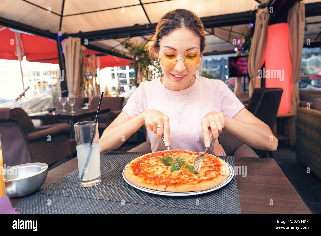 Young girl eating delicious pizza with cheese and greens in pizzeria Stock Photo