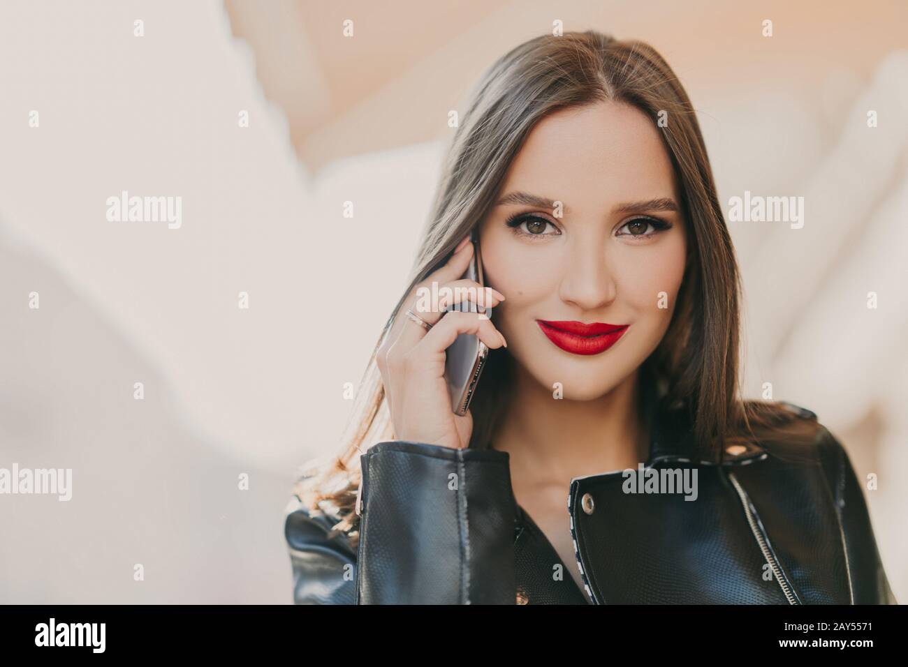 Close up shot of lovely woman talks with friend via mobile app, has makeup  and red lips, dressed in leather jacket, has spare time outdoor. Online com  Stock Photo - Alamy