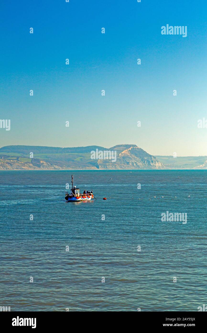 A fishing boat in Lyme Bay on the Jurassic Coast with Golden Cap beyond, viewed from Lyme Regis, Dorset, England, UK Stock Photo