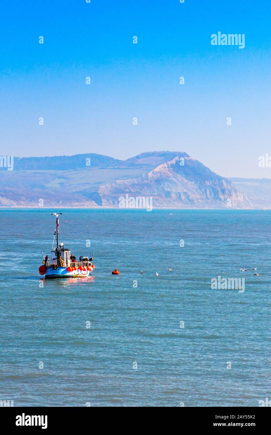 A fishing boat in Lyme Bay on the Jurassic Coast with Golden Cap beyond, viewed from Lyme Regis, Dorset, England, UK Stock Photo