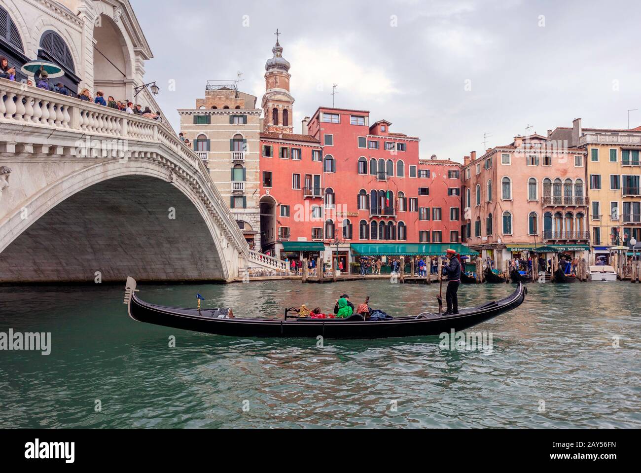 A gondola carrying tourists passes through Rialto bridge on the Grand Canal Stock Photo