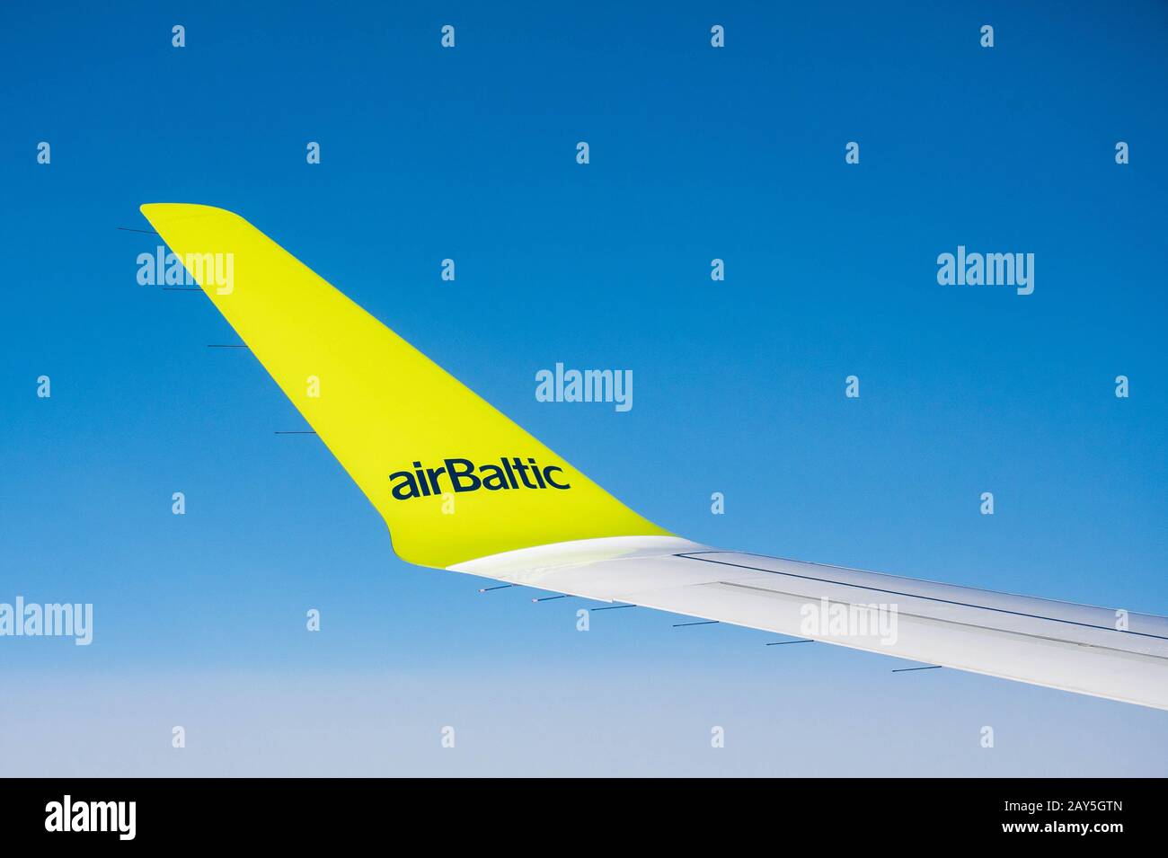 Part of a wing of the Boeing of Air Baltic airlines against the background of the blue sky during flight Stock Photo