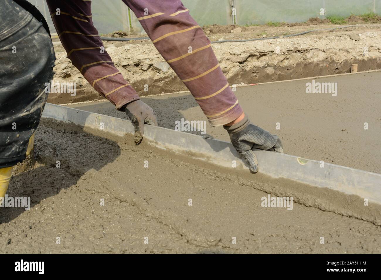 Bricklayer pulls off concrete with long aluminium lath - close-up Stock Photo