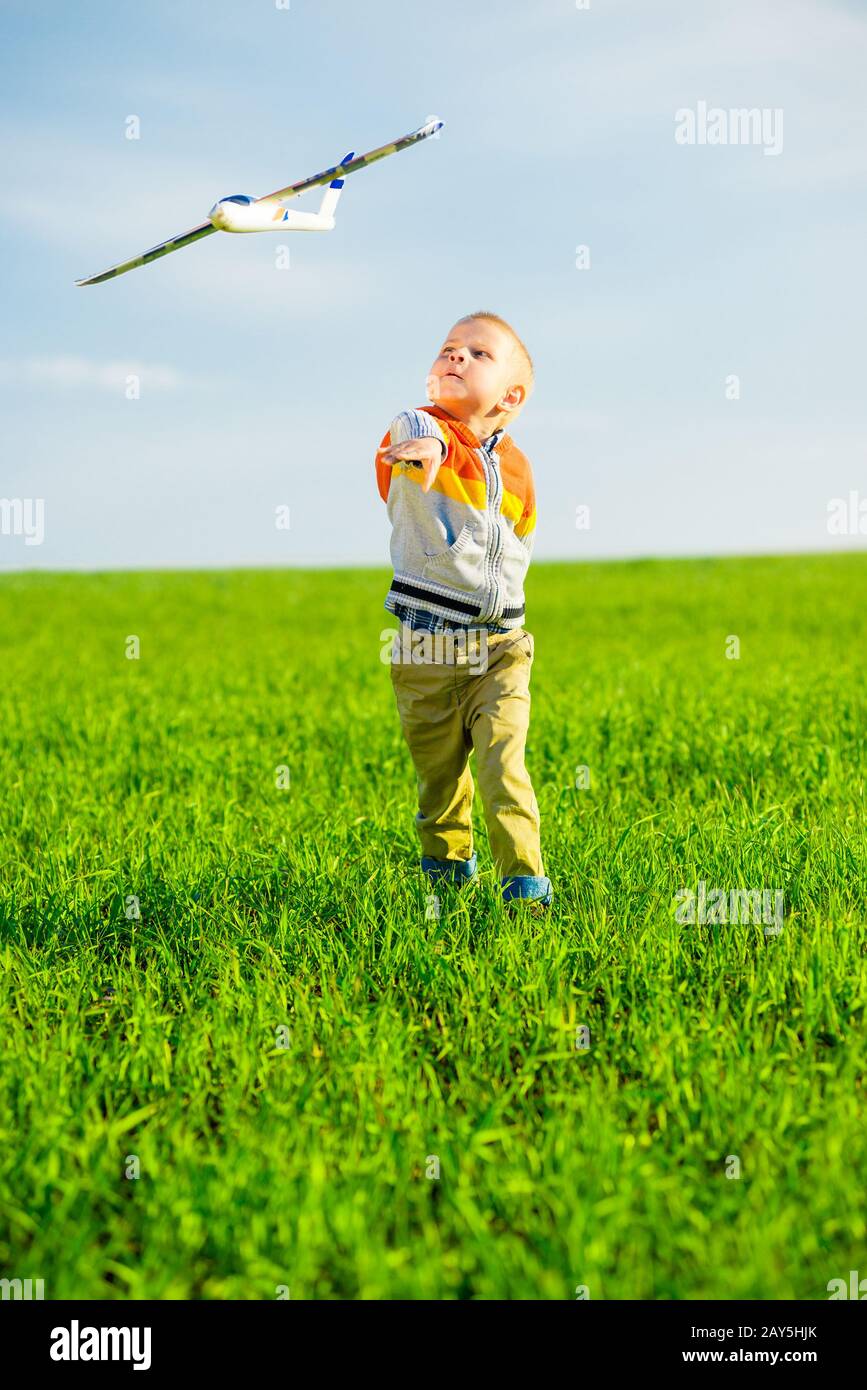 Happy boy playing with toy airplane against blue summer sky and green ...