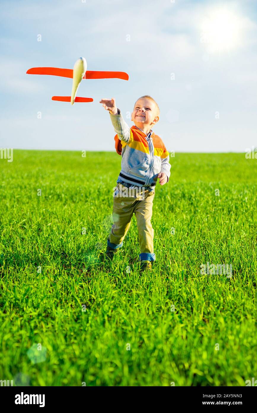 Happy boy playing with toy airplane against blue summer sky and green ...