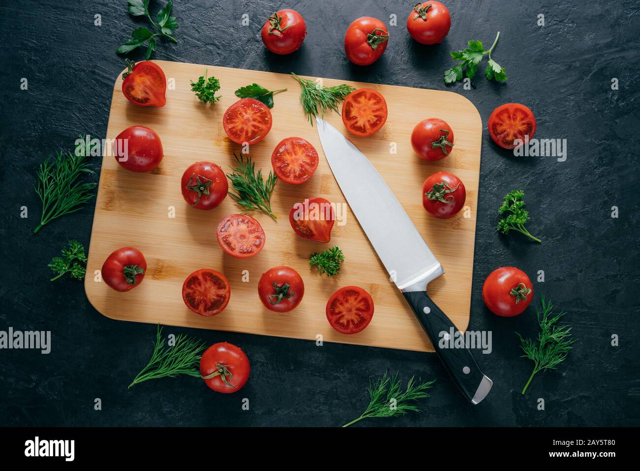 Cherry red tomatoes slices with knife on chopping board for making ketchup. Organic vegetables for making tasty full of vitamins salad. Vegetarian dis Stock Photo