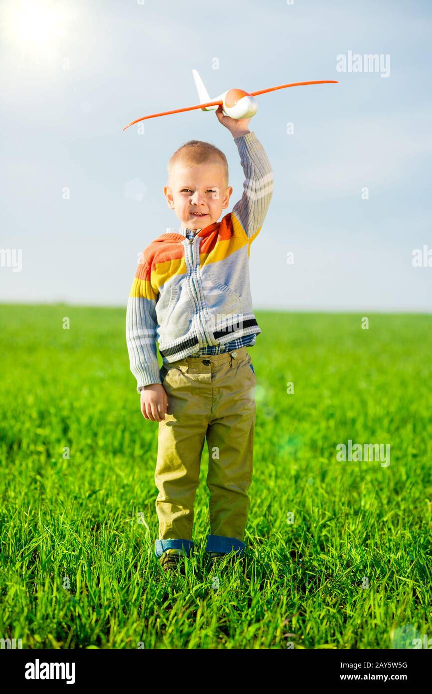 Happy boy playing with toy airplane against blue summer sky and green ...