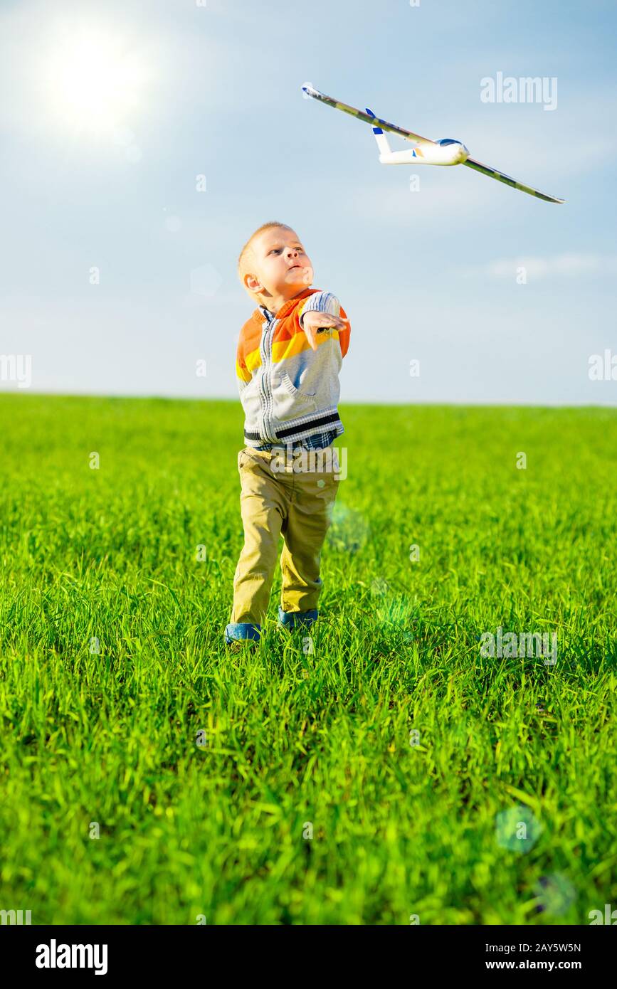 Happy boy playing with toy airplane against blue summer sky and green ...