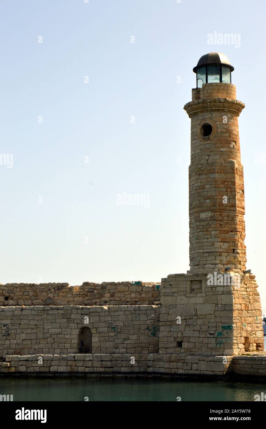 Marine lighthouse in a port of Crete with ramparts and the ocean Stock