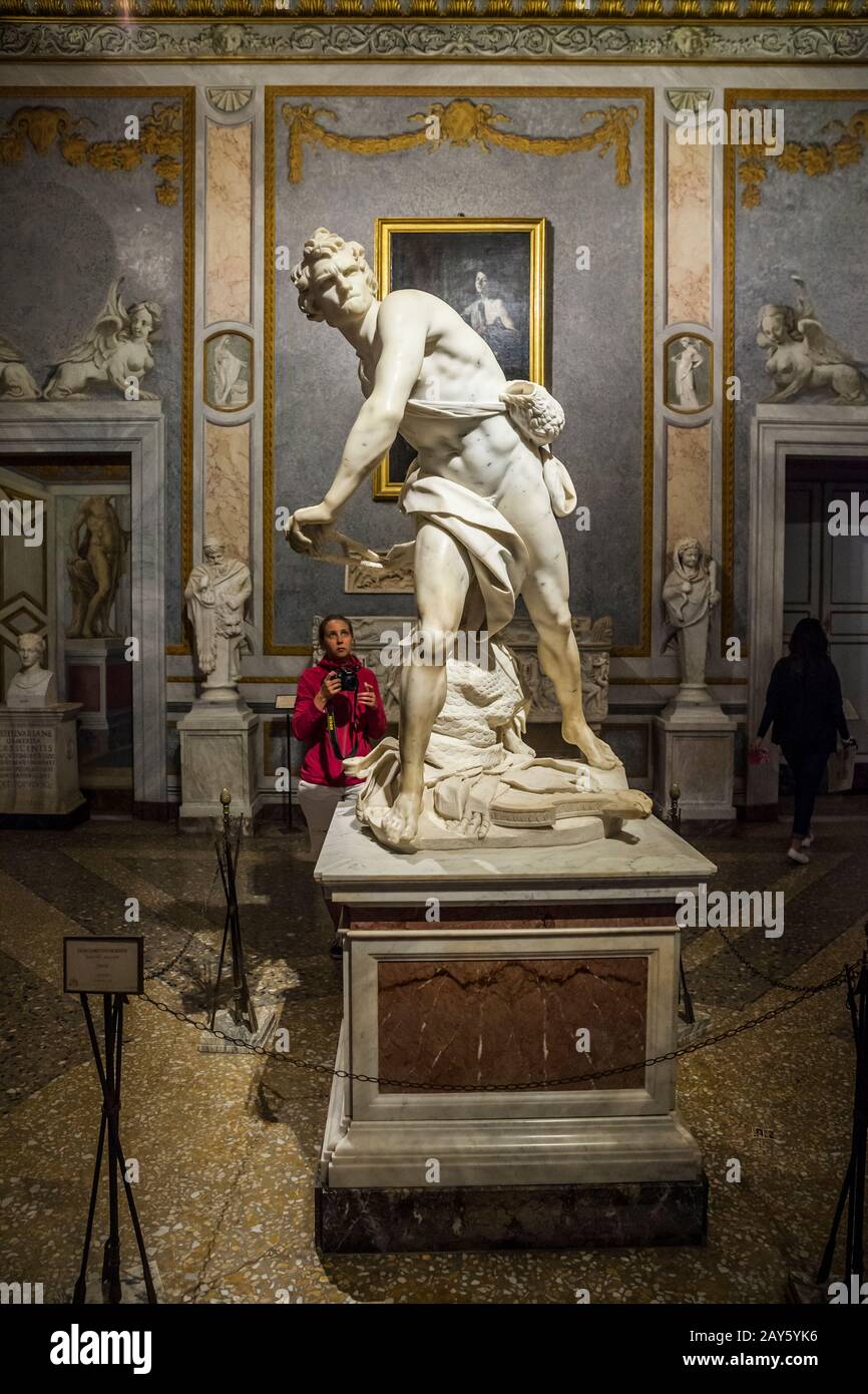A woman tourist contemplates taking a picture of a famous sculpture of David created by Gian Lorenzo Bernini, Borghese Gallery, Rome, Italy. Stock Photo