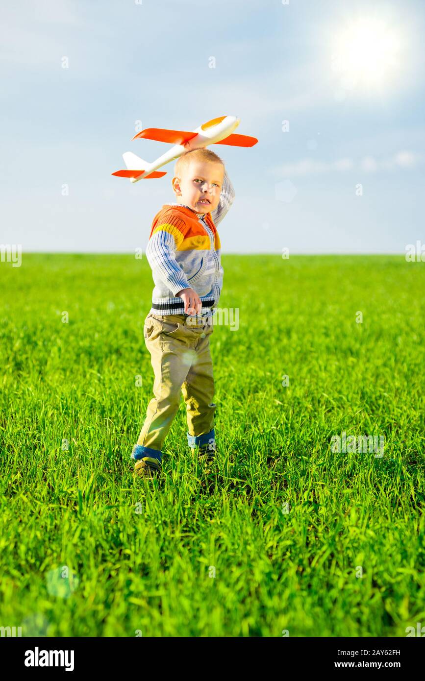 Happy boy playing with toy airplane against blue summer sky and green ...