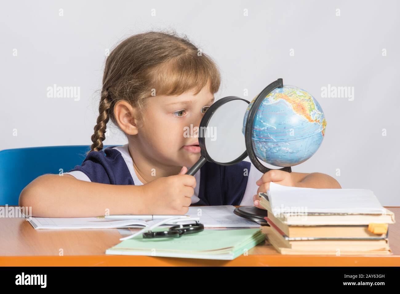 Six-year girl sitting at the table and looks at the globe through a magnifying glass Stock Photo