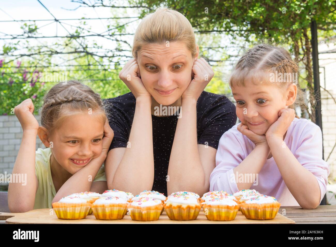 Mother and two daughters with a good appetite and big eyes looking at easter cupcakes Stock Photo