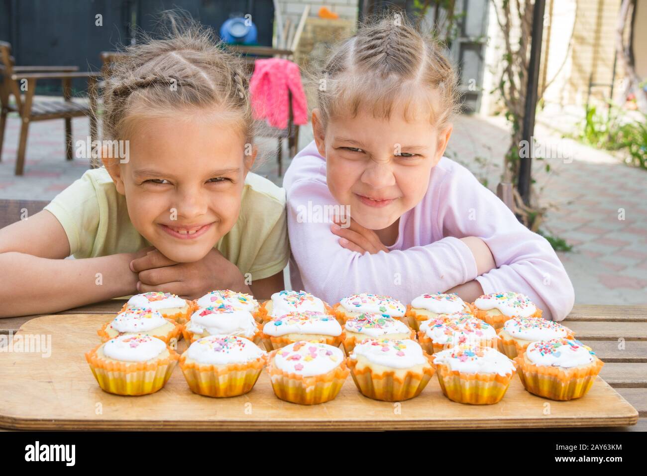 Two girls pretending funny faces, sitting in front of easter cupcakes Stock Photo