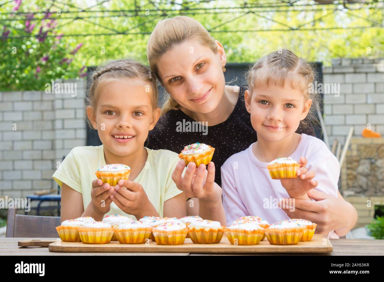 Mother and two daughters sitting at the table with Easter cupcakes in his hands and looked into the frame Stock Photo