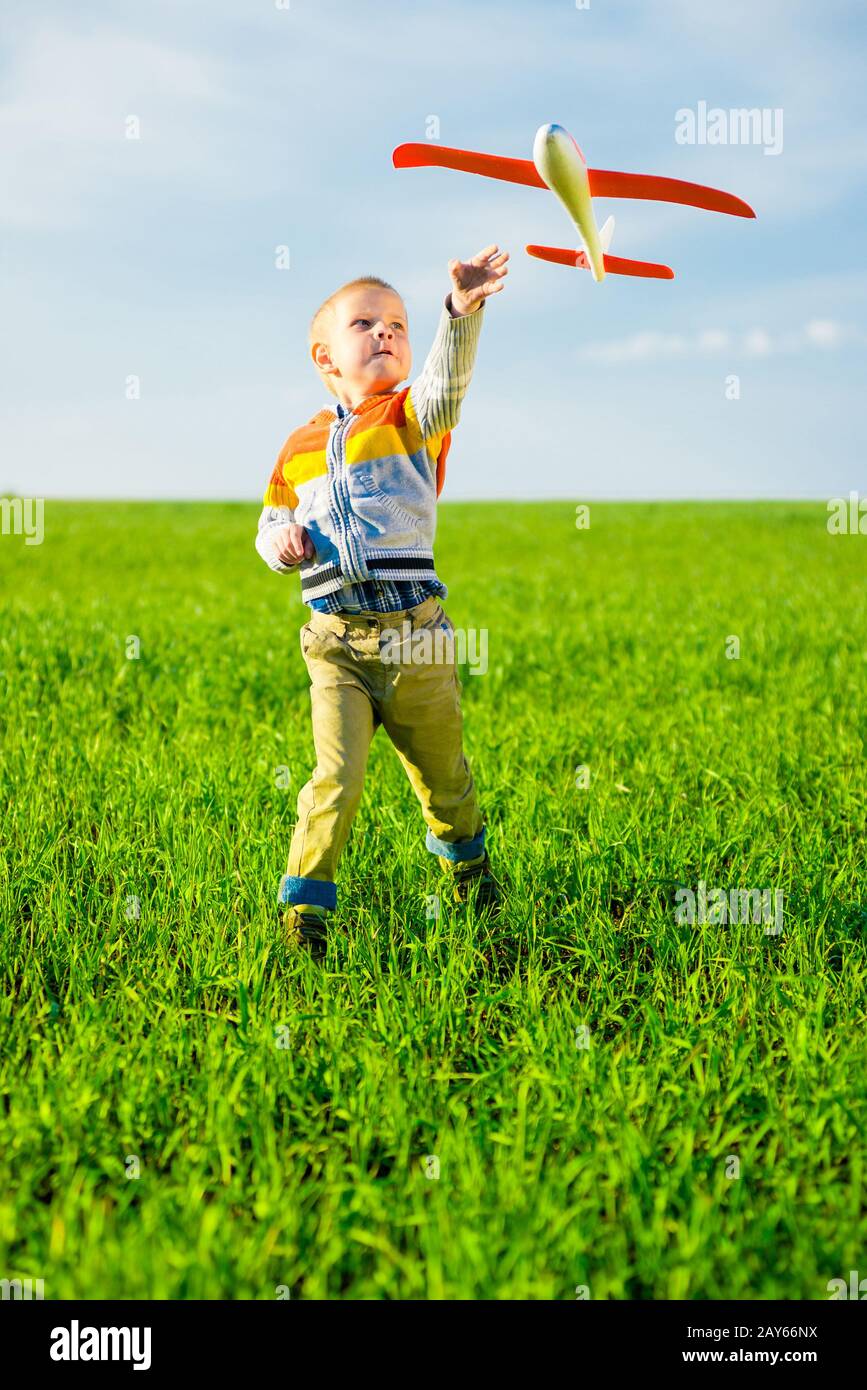 Happy boy playing with toy airplane against blue summer sky and green ...