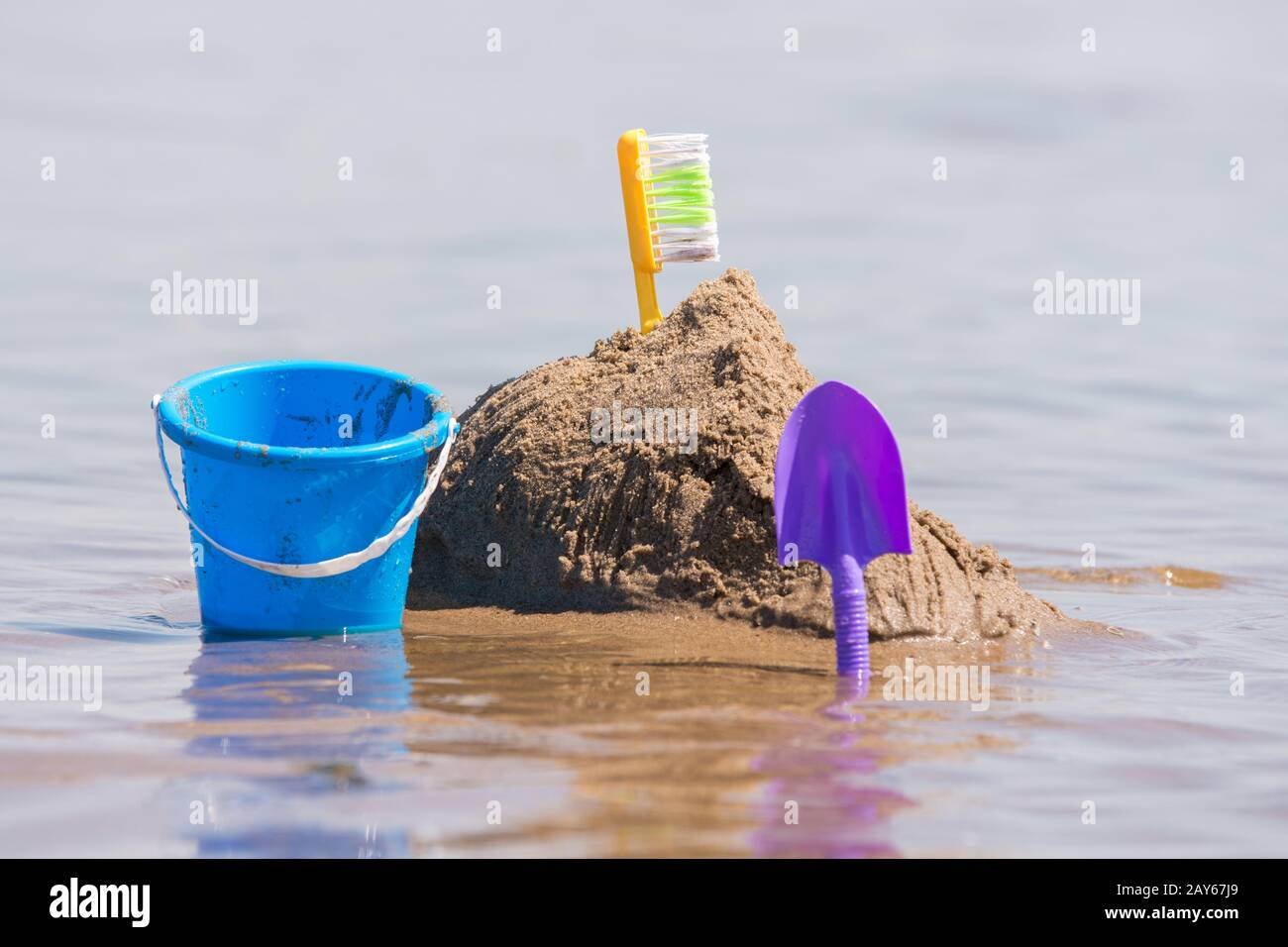 Construction of a sand castle, next to which stands a shovel and bucket on the shallows of the river Stock Photo