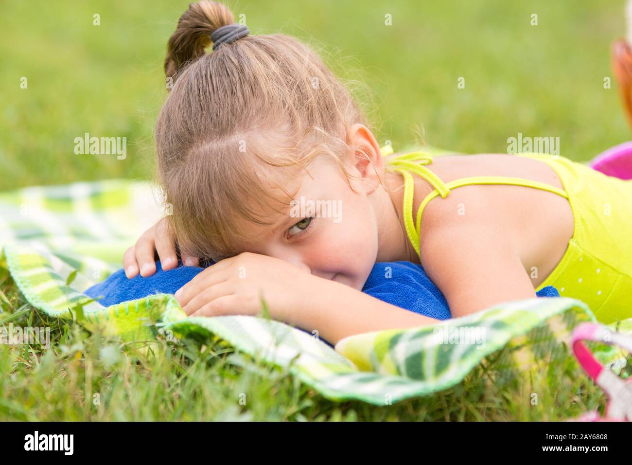 Five-year girl lies on a bed on a green meadow and artfully looks aside Stock Photo