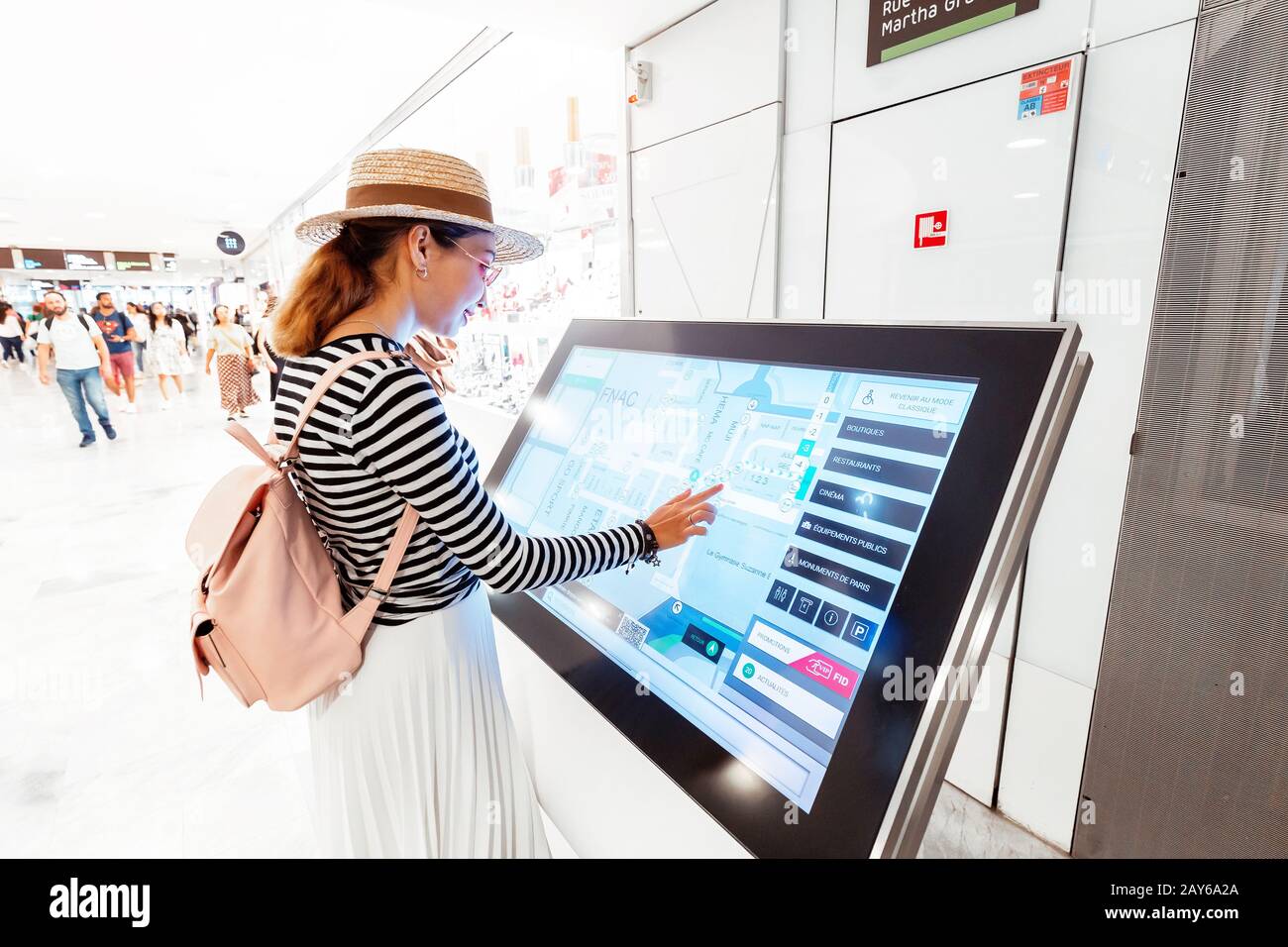 28 July 2019, Paris, France: Asian girl uses touchscreen terminal to find the right boutique in a big shopping Mall Stock Photo