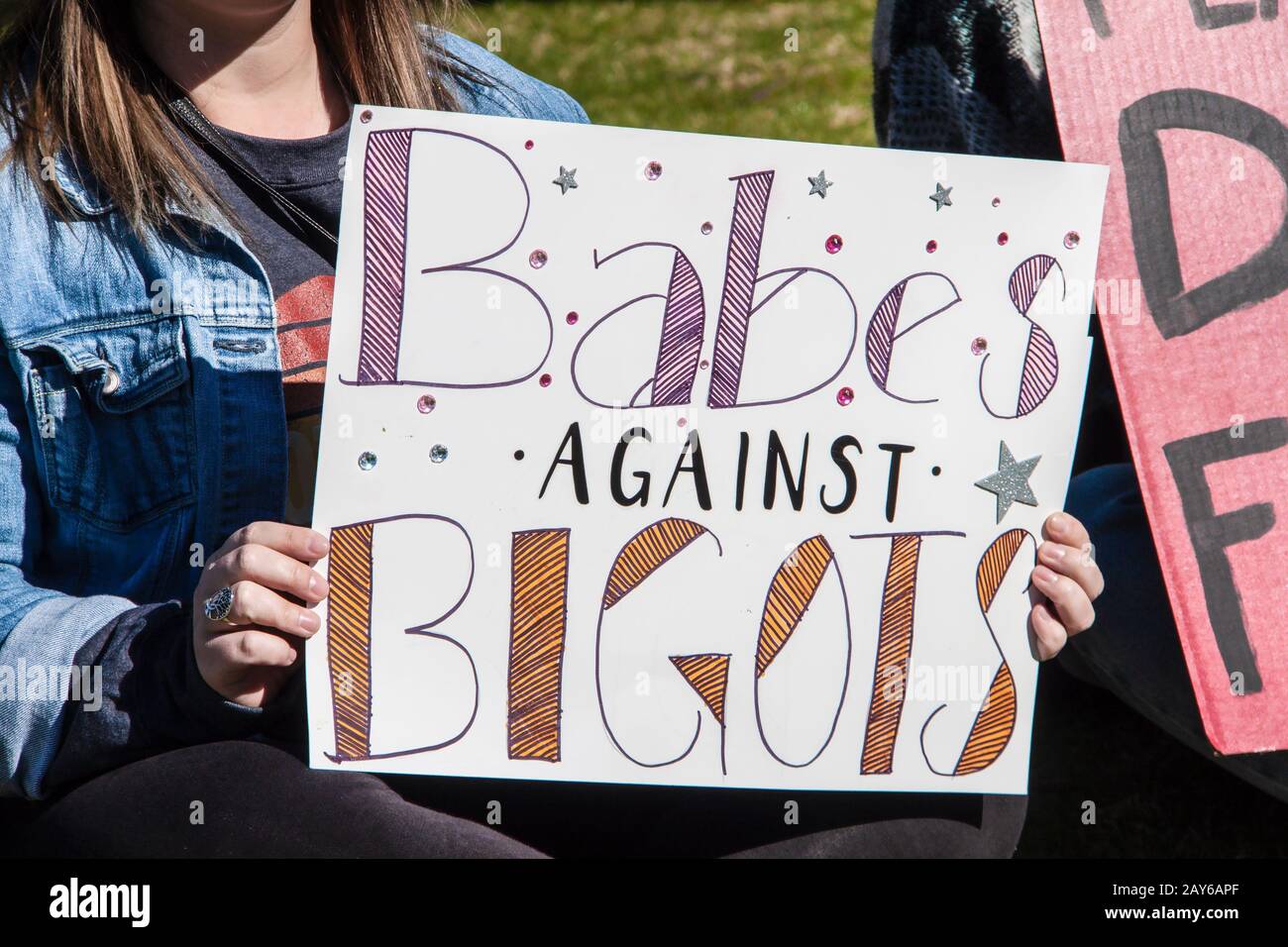 Girl in jeans jacket holding homemade sign - Babes against Bigots - with stars and jewels on it Stock Photo