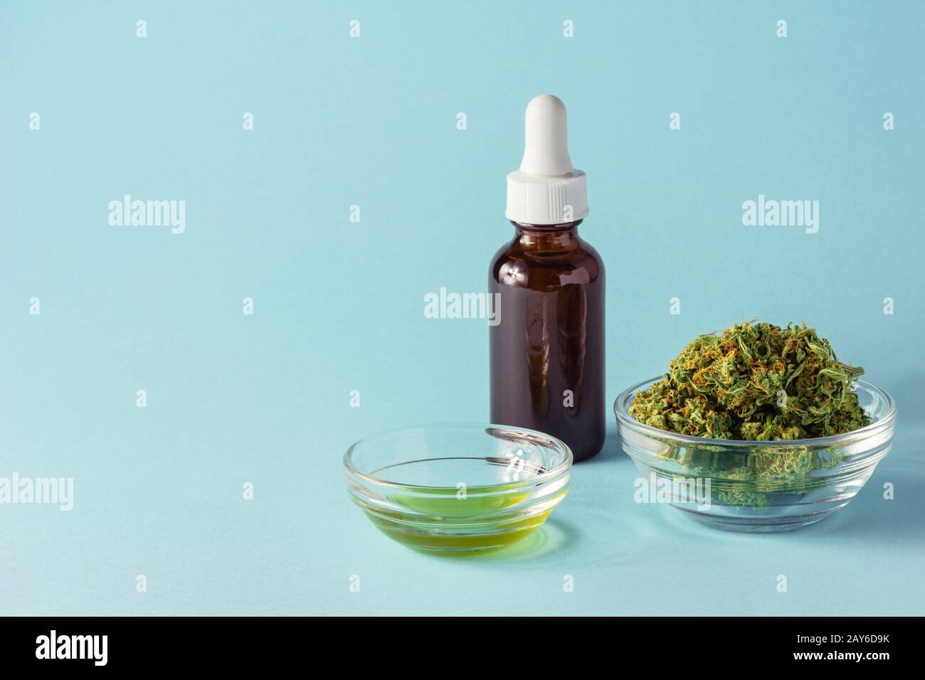 Glass Bottle and Dish of CBD or THC Oil with Hemp or Cannabis Buds on Aqua Blue Background Stock Photo