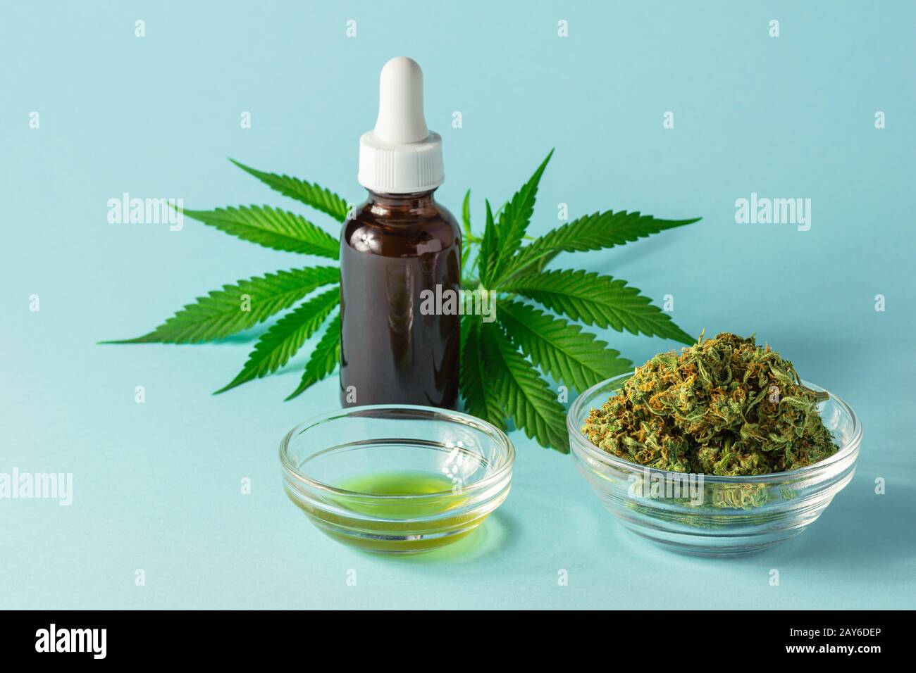 Glass Bottle of CBD or THC Oil with Hemp or Cannabis Buds, Oil, and Pot Leaves on Aqua Blue Background Stock Photo