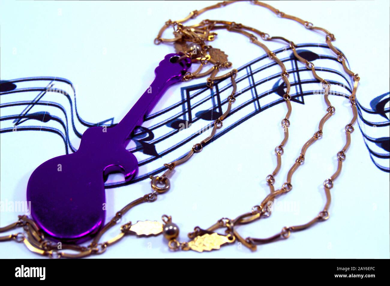 Guitar of mauve color with a chain rests on musical notes. Stock Photo