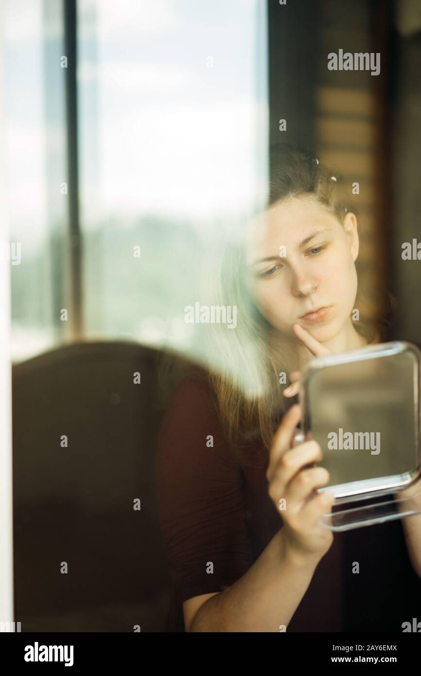 Young woman standing by the window with a mirror in her hands Stock Photo