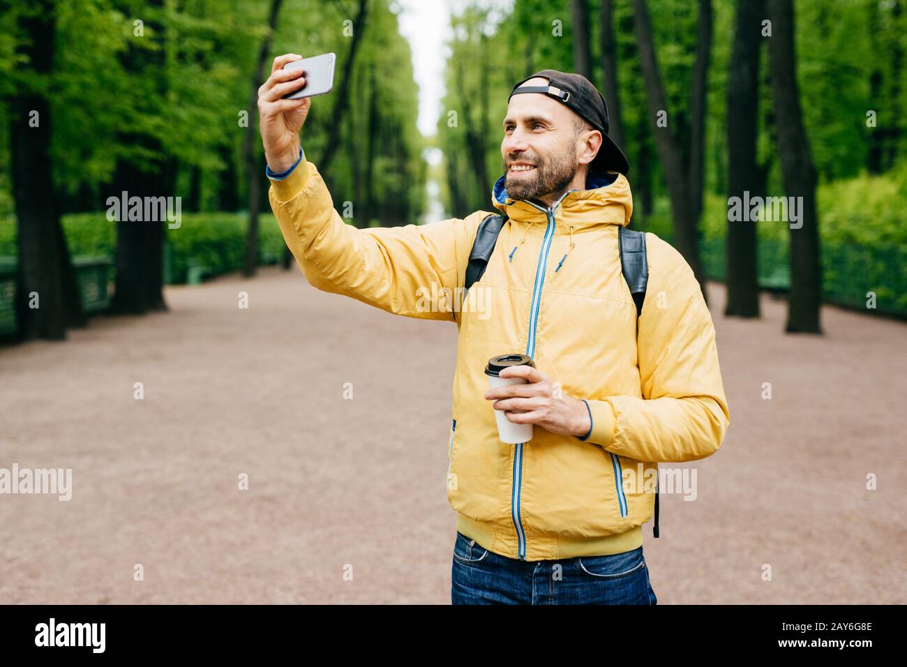 Isolated portrait of hipster guy wearing fashionable clothes resting in park alone admiring good weather and fresh air. Bearded man making selfie in p Stock Photo