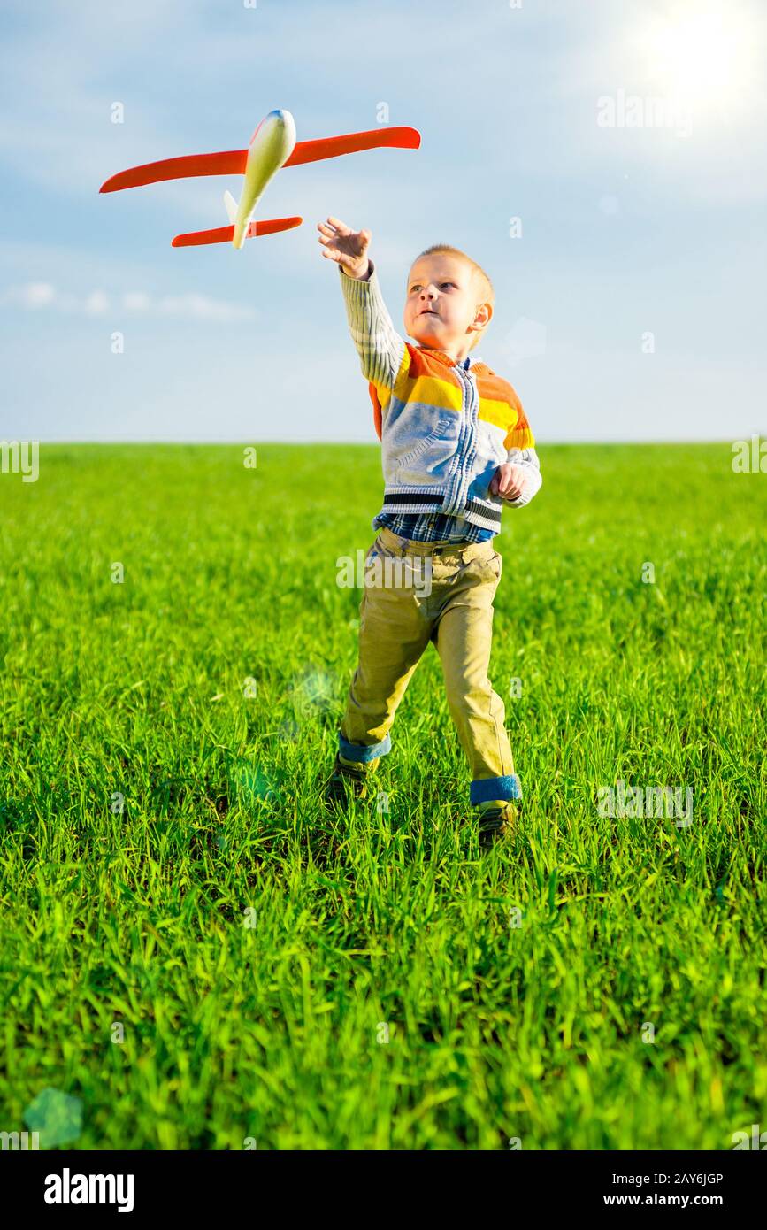Happy boy playing with toy airplane against blue summer sky and green ...