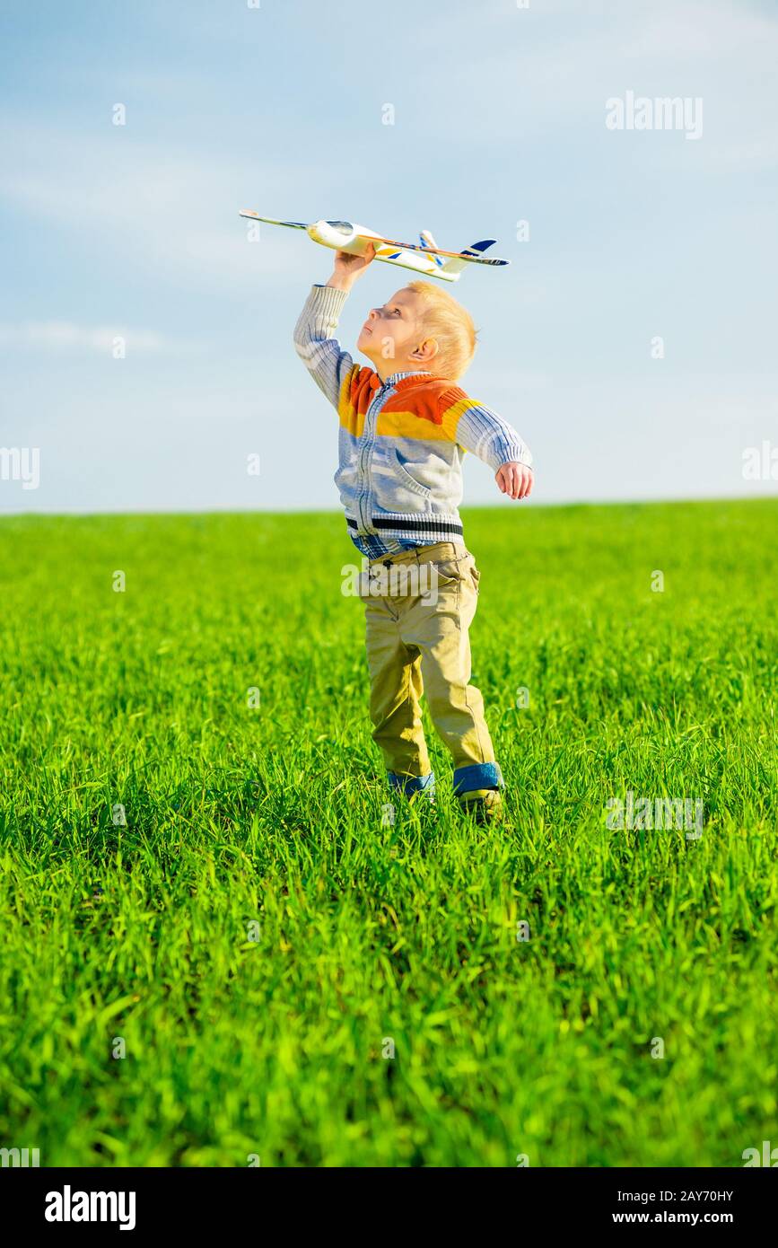 Happy boy playing with toy airplane against blue summer sky and green ...