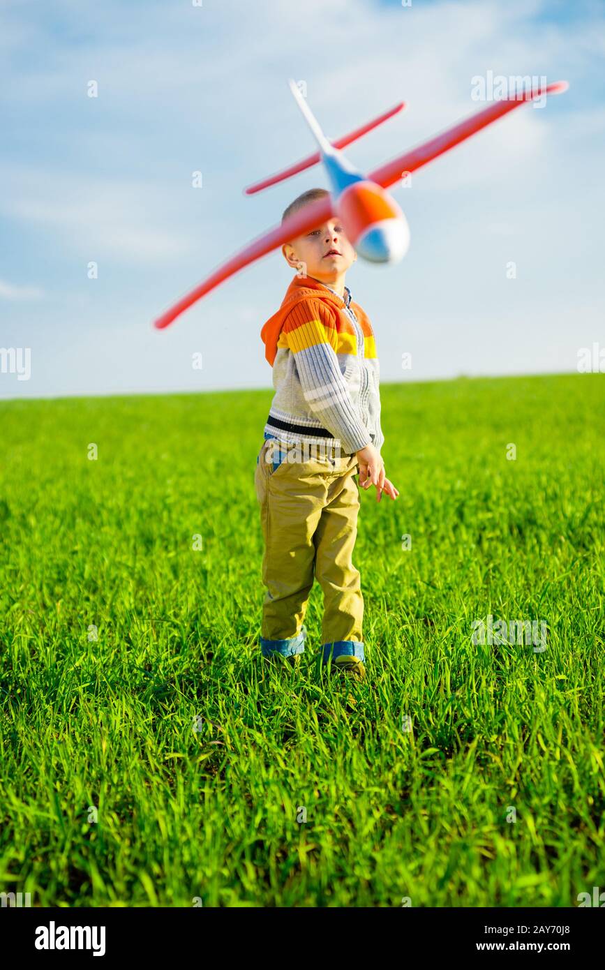 Happy boy playing with toy airplane against blue summer sky and green ...