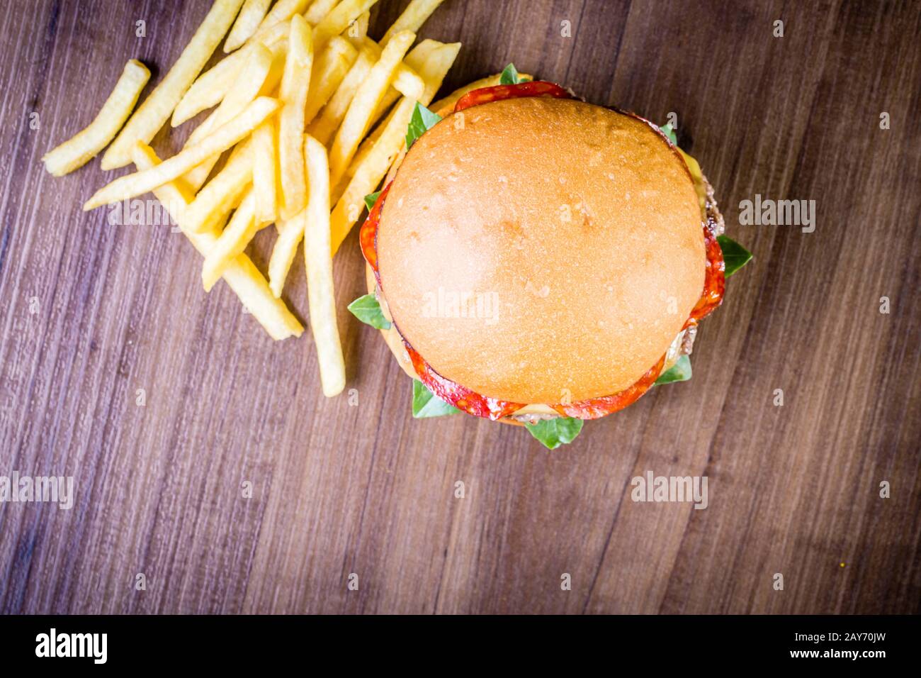 Craft beef burger with cheese, italian peperoni, tomato, basil leafs and french fries on wood table and rustic background Stock Photo