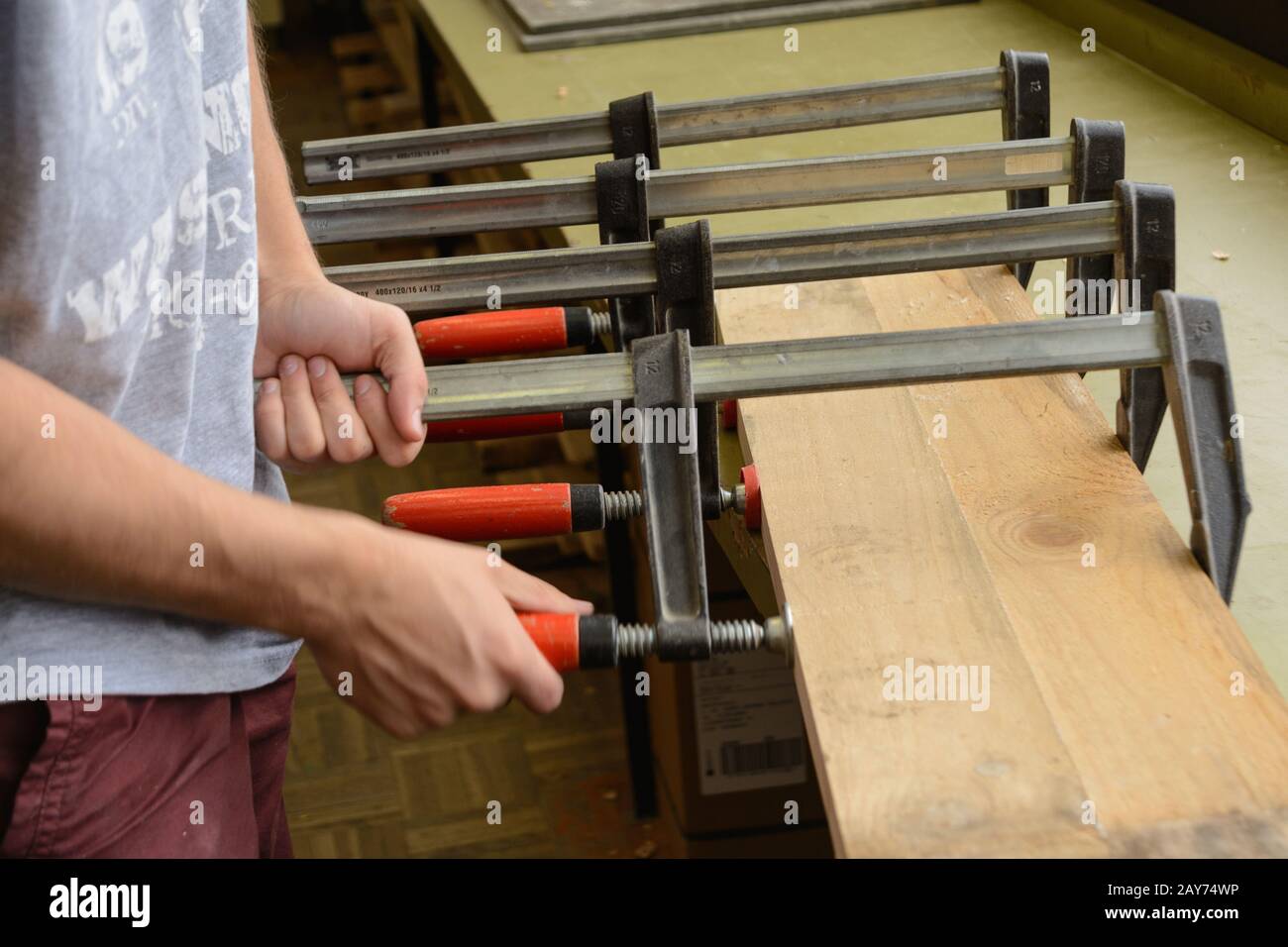 Joiner presses glued wooden board with a screw clamp - close-up Stock Photo