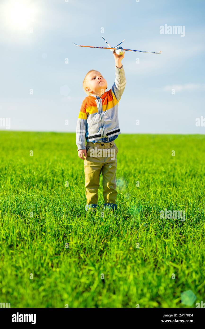 Happy boy playing with toy airplane against blue summer sky and green ...