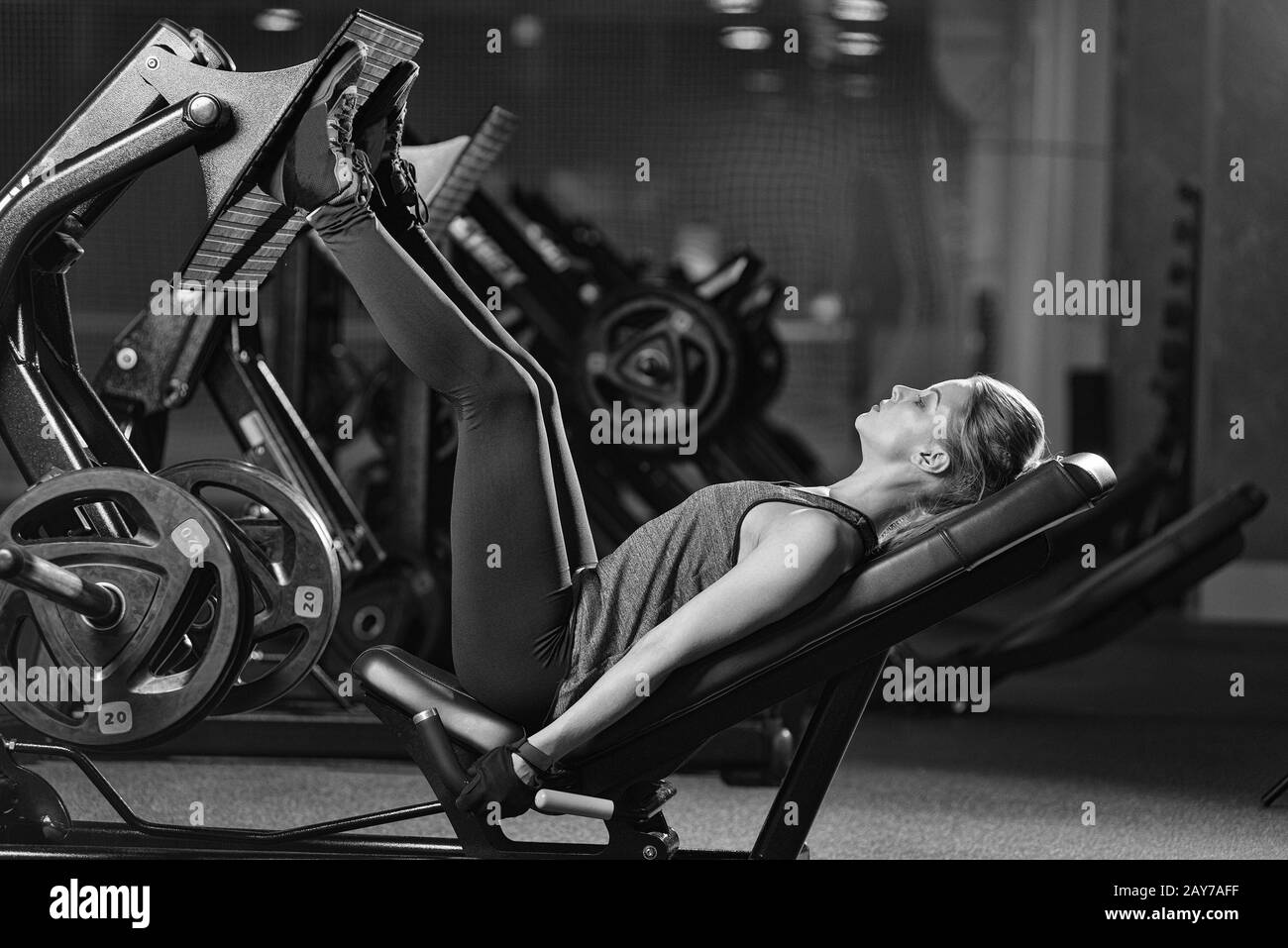 Sportive woman using weights press machine for legs. Gym. Stock Photo