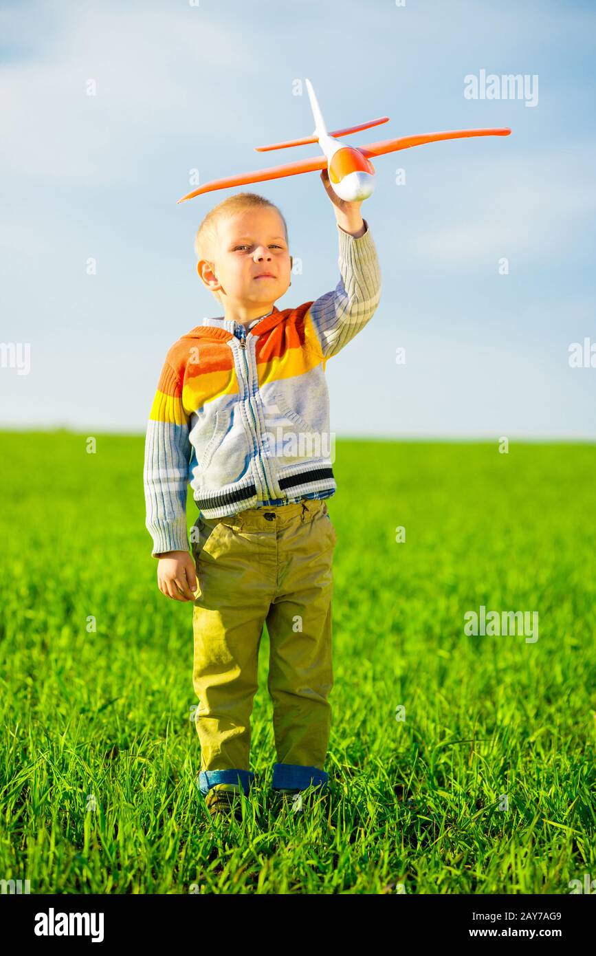 Happy boy playing with toy airplane against blue summer sky and green ...