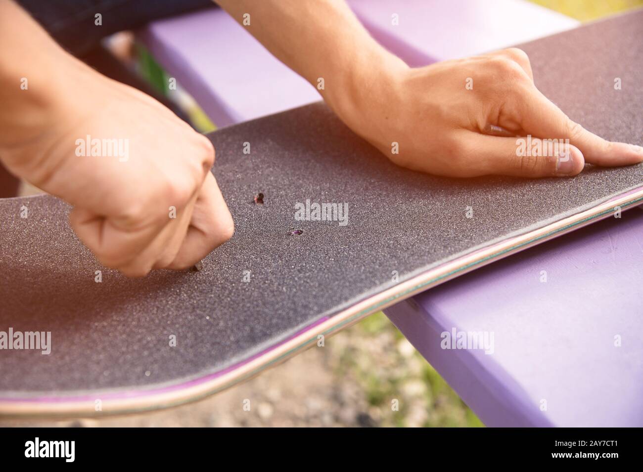 Boy makes bolt holes on the griptape on a skateboard Stock Photo